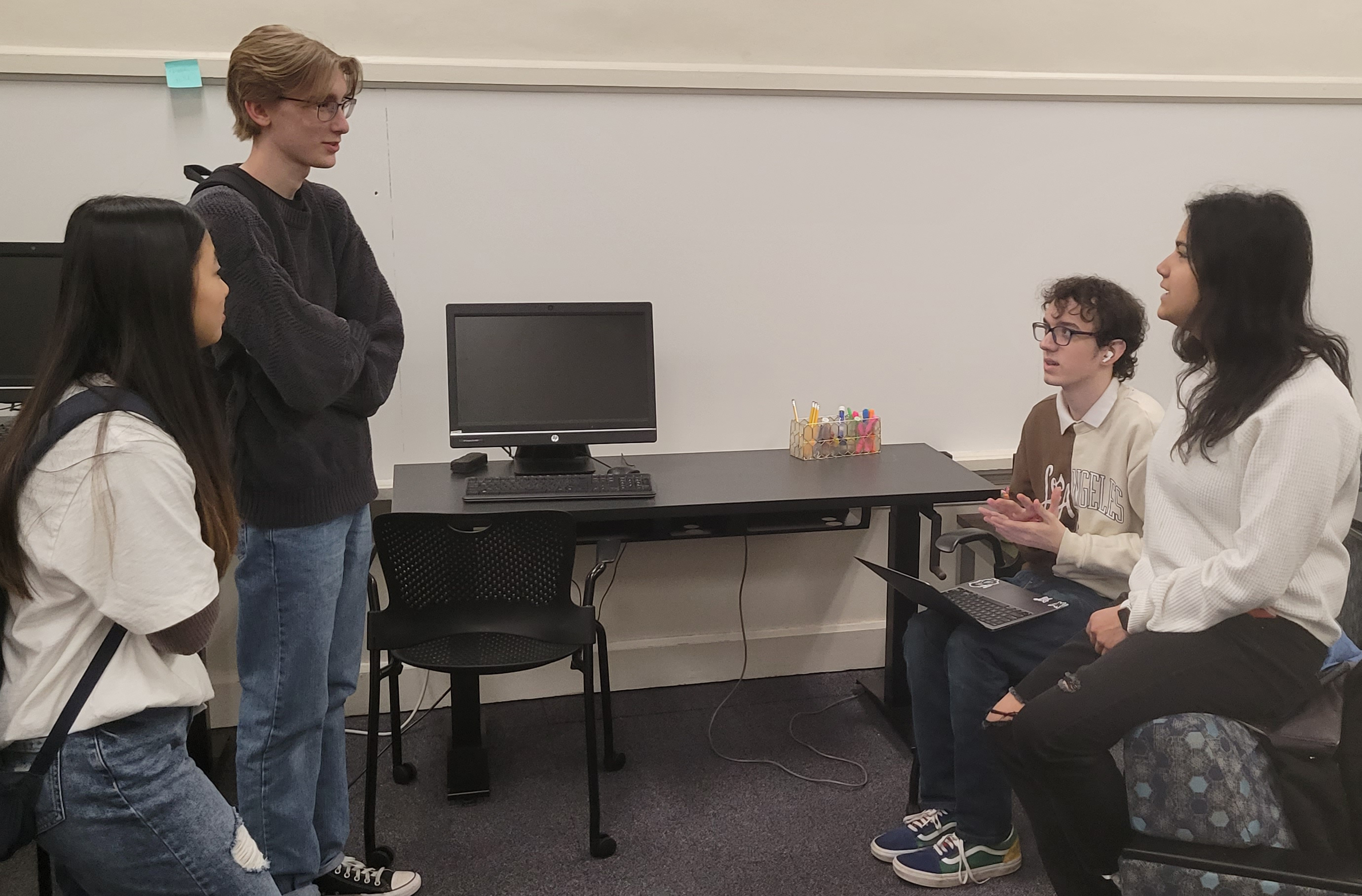 Four students gathering around a black desk talking with a lap top open